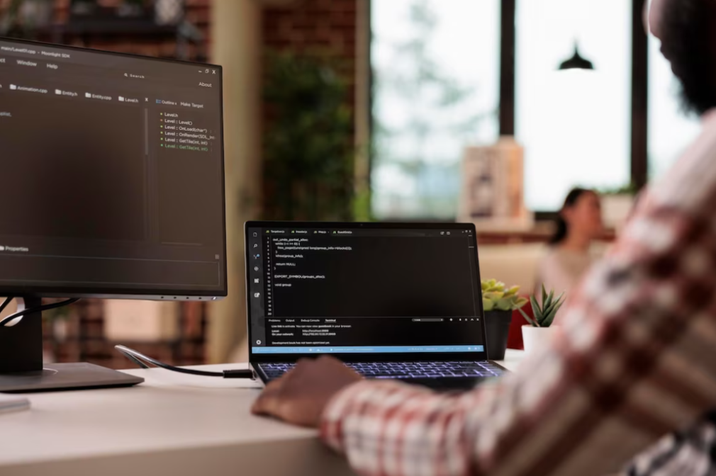 man in shirt sitting at the table and looking gat the laptop with coding on it